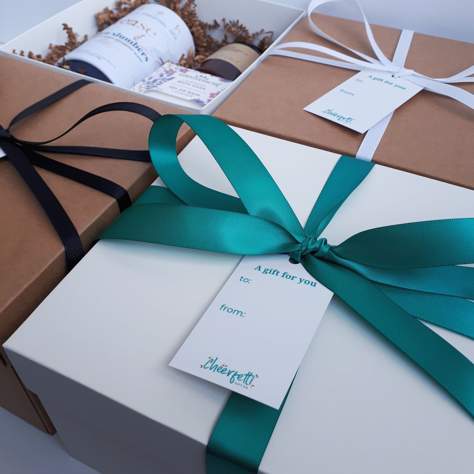 Build Your Own Gift Box with Cheerfetti Gift Co. Three gift boxes with different box and ribbon colour options, and a fourth showing some gifts inside.