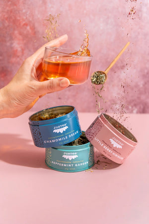 Justea Herbal Tea Trio spilling out with glass of tea in person's hand