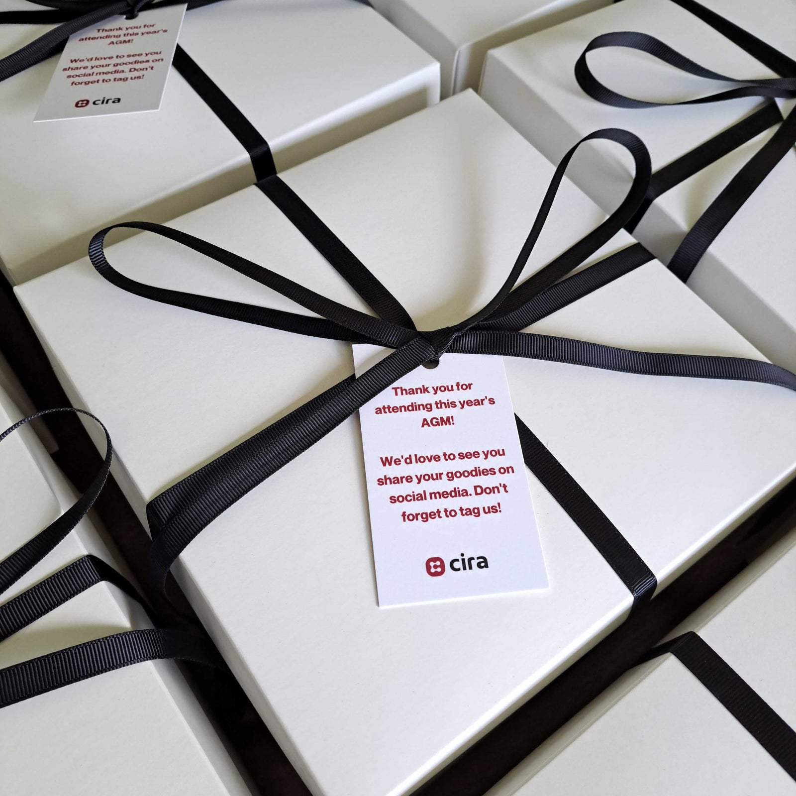 White corporate gift boxes wrapped with black ribbon and custom gift tags for corporate events