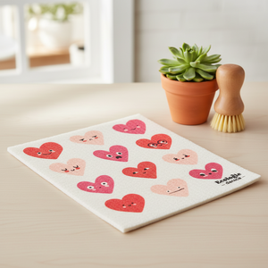 Dishcloth with heart designs on a table next to a potted plant and brush