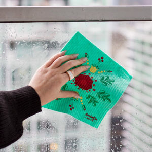 Person using a green reusable dishcloth with floral design to clean a window