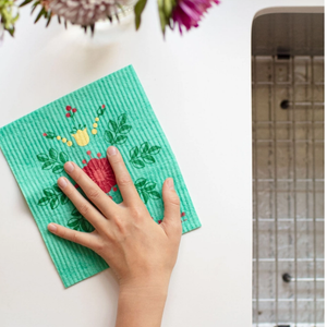 Green dishcloth with floral design held by a hand on a white surface.