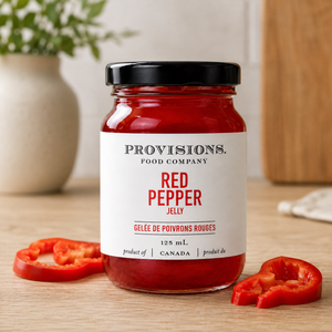 Provisions Red Pepper Jelly on kitchen table beside red peppers