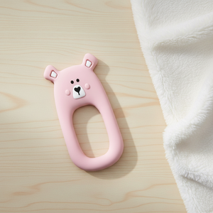Pink bear silicone teether Little Cheeks on table beside blanket