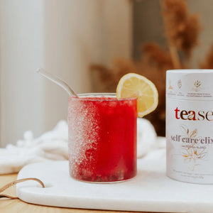 Tease Self Care Elixir to the right of glass with lemon and straw